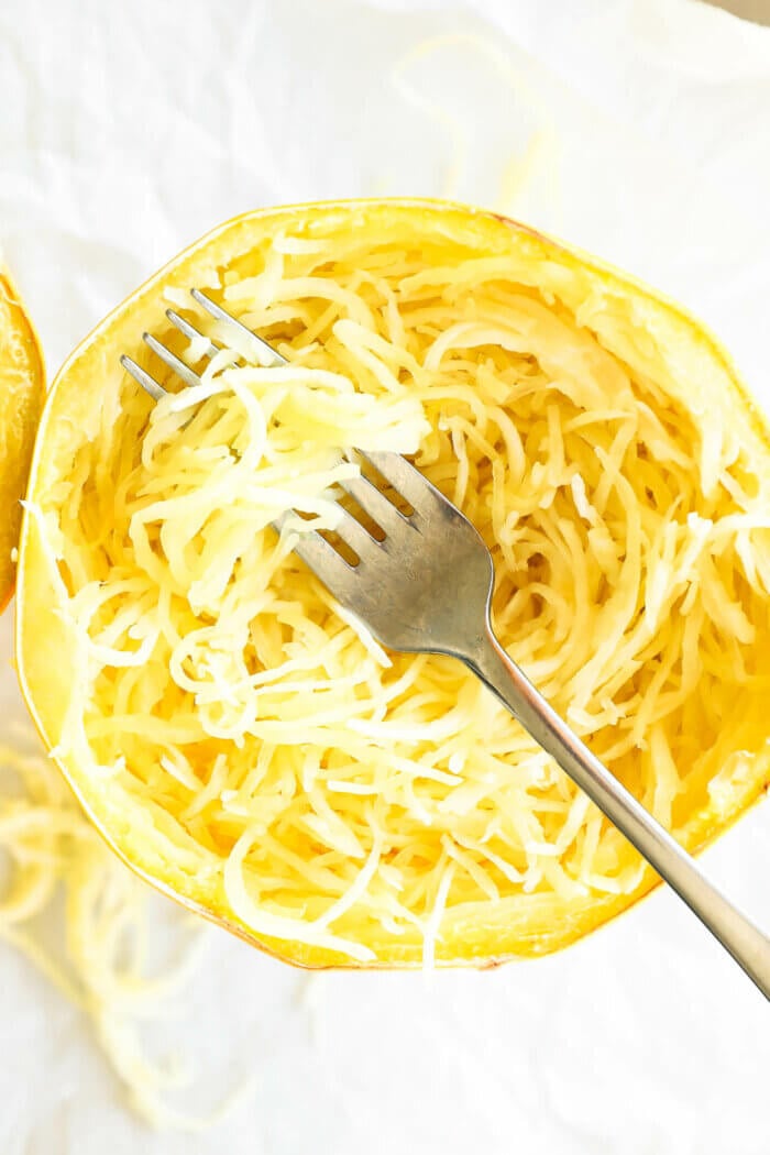 Spaghetti squash noodles all scooped out in the shell with a fork with noodles wrapped around it.