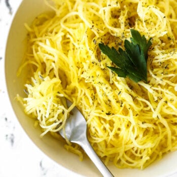 Overhead image of a bowl full of spaghetti squash noodles with herbs sprinkled on top. A fork is in the bowl with noodles wrapped around it.