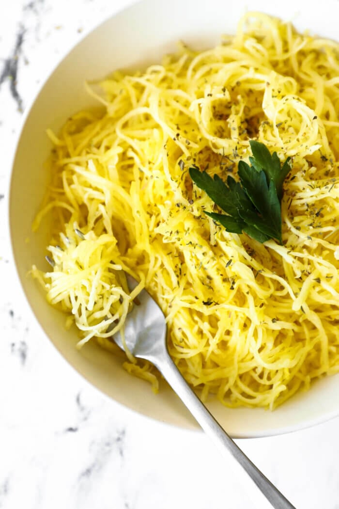 Overhead image of a bowl full of spaghetti squash noodles with herbs sprinkled on top. A fork is in the bowl with noodles wrapped around it. 