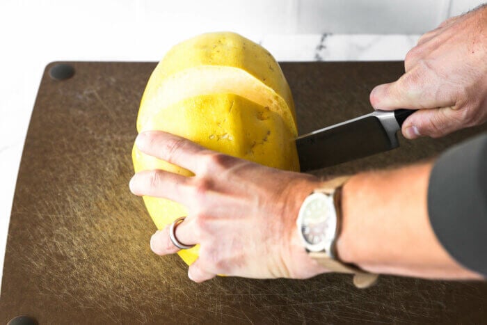 Image of someone cutting a spaghetti squash crosswise with a large chef's knife.