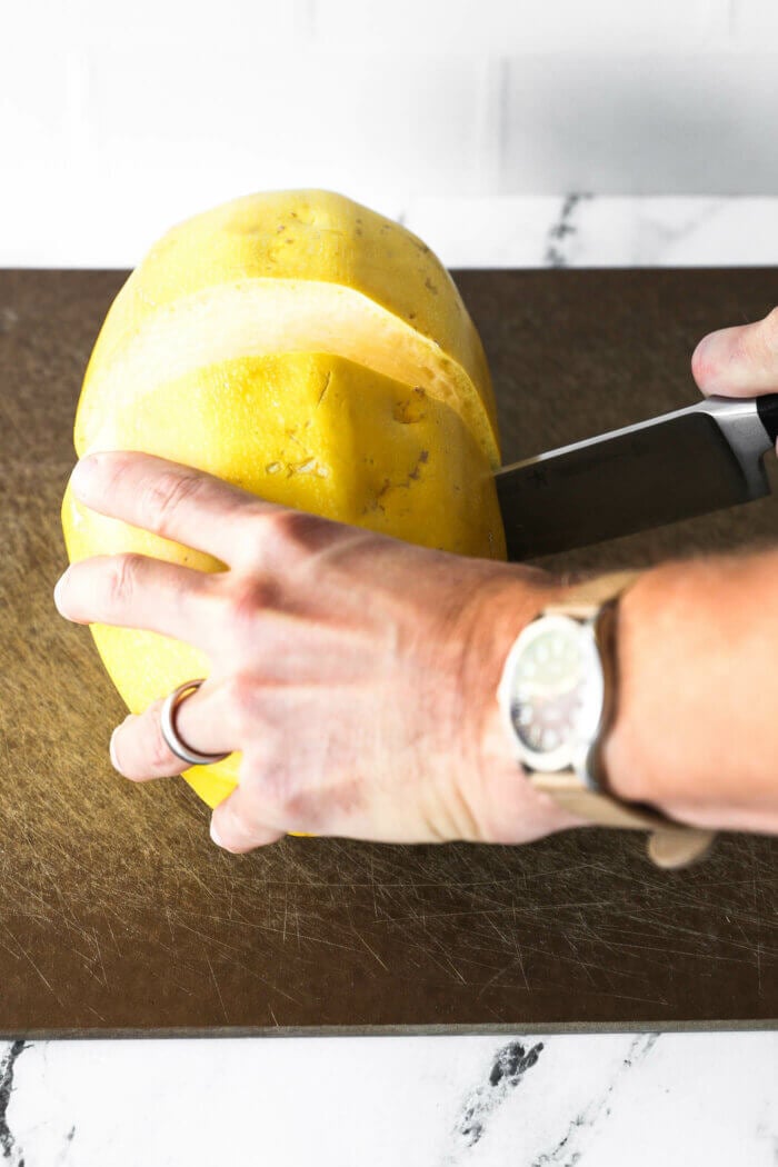 Image of someone cutting a spaghetti squash crosswise with a large chef's knife.