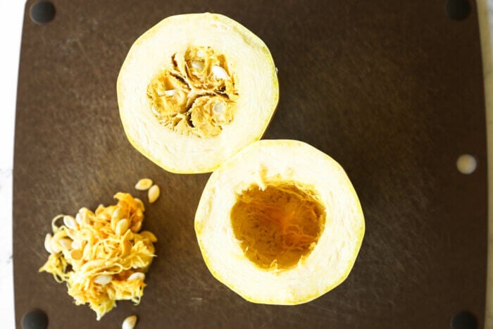 Image of spaghetti squash cut in half crosswise with the seeds scooped out of one side and in a pile on the cutting board.