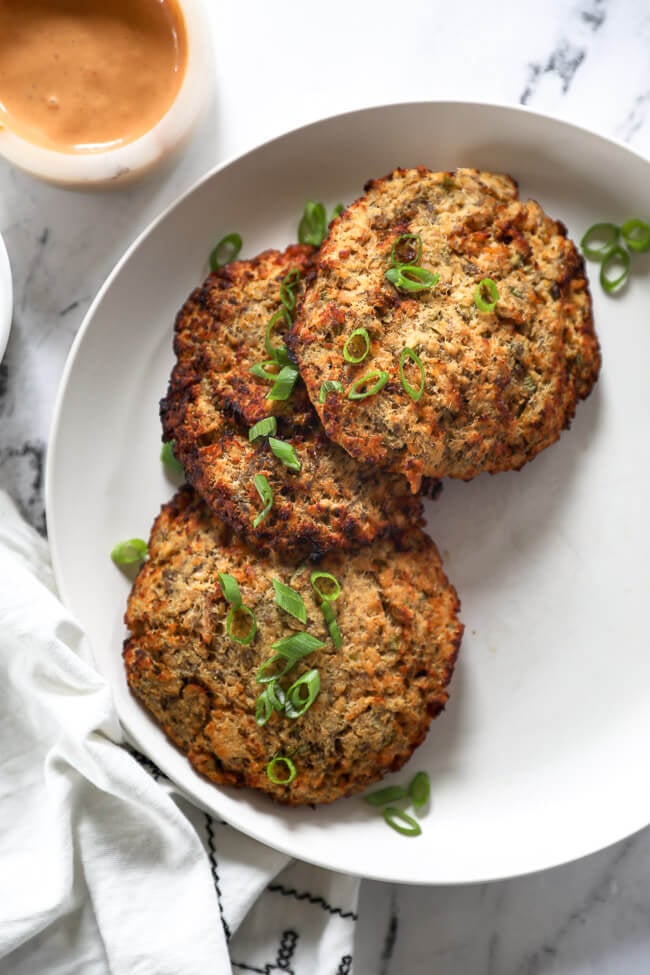 Three air fryer salmon patties on a plate with sliced green onions on top