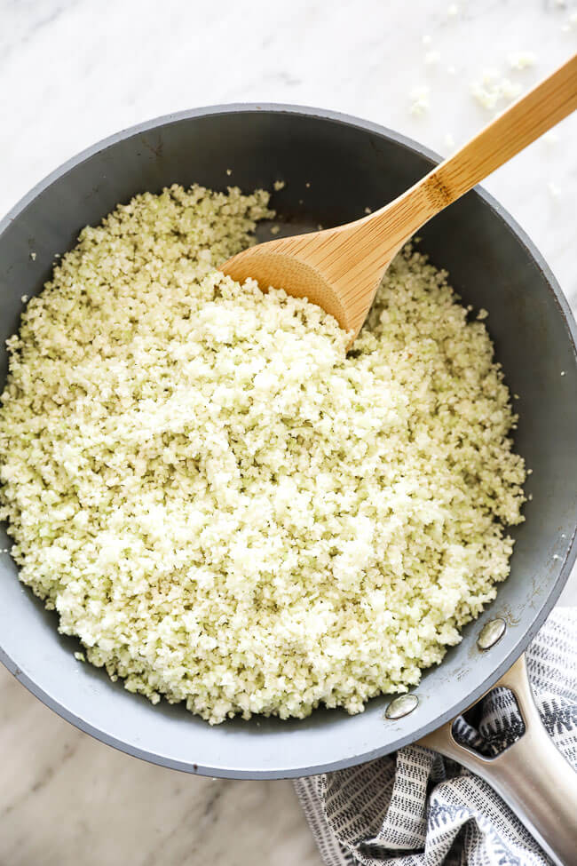 Vertical overhead image of cauliflower rice in a skillet with a serving spoon. 
