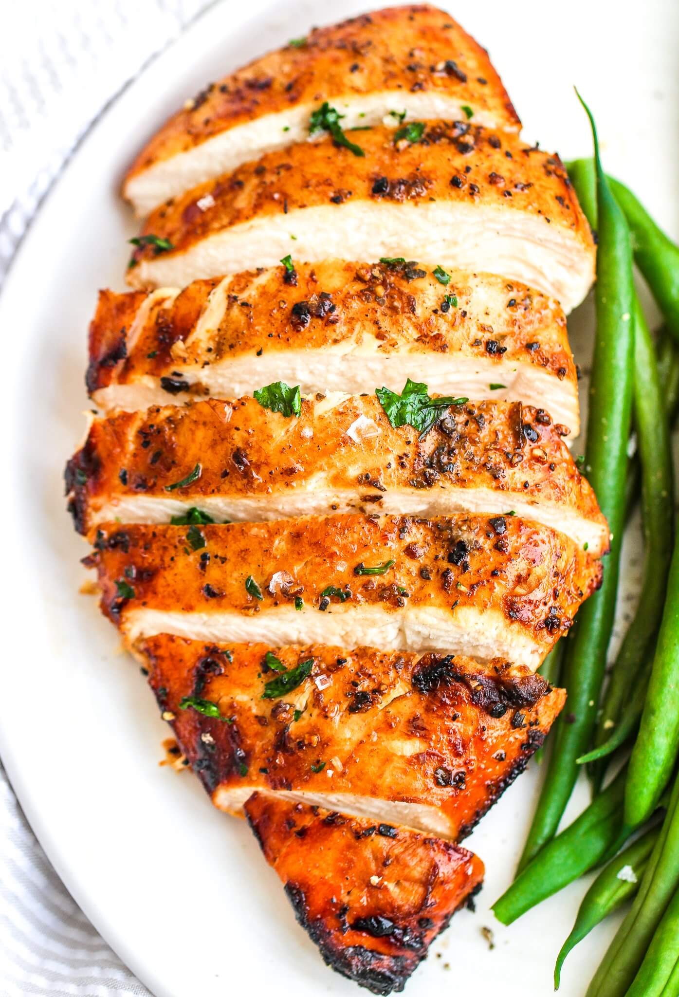 Close up of sliced chicken breast with seasonings and green beans on side
