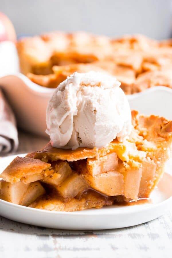 Slice of paleo apple pie with scoop of white ice cream on top. Pie in background