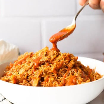 Bowl of shredded instant pot buffalo chicken with sauce pouring in from a spoon