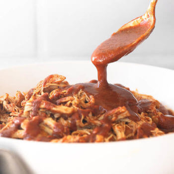 Instant pot BBQ shredded chicken in a bowl with a spoon pouring BBQ sauce on top