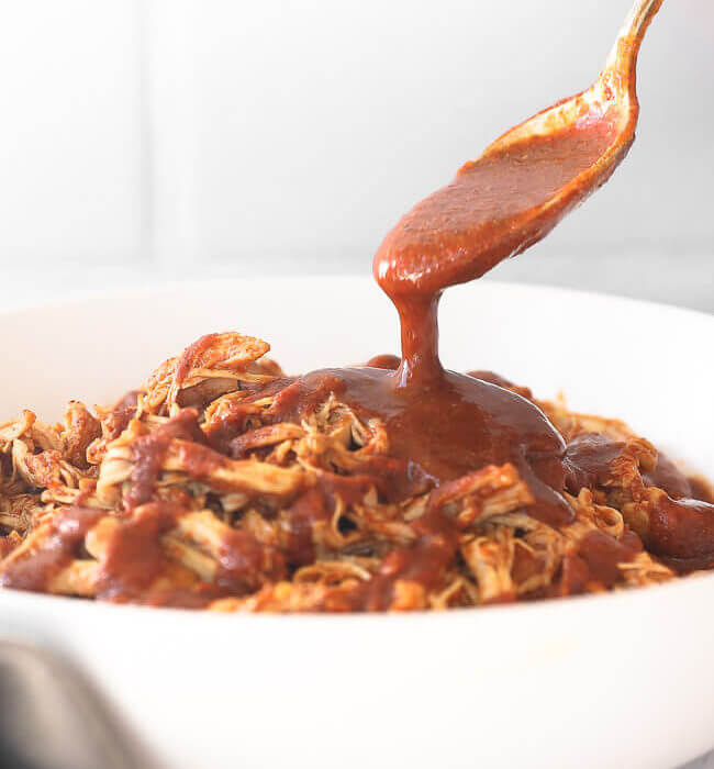 Instant pot BBQ shredded chicken in a bowl with a spoon pouring BBQ sauce on top