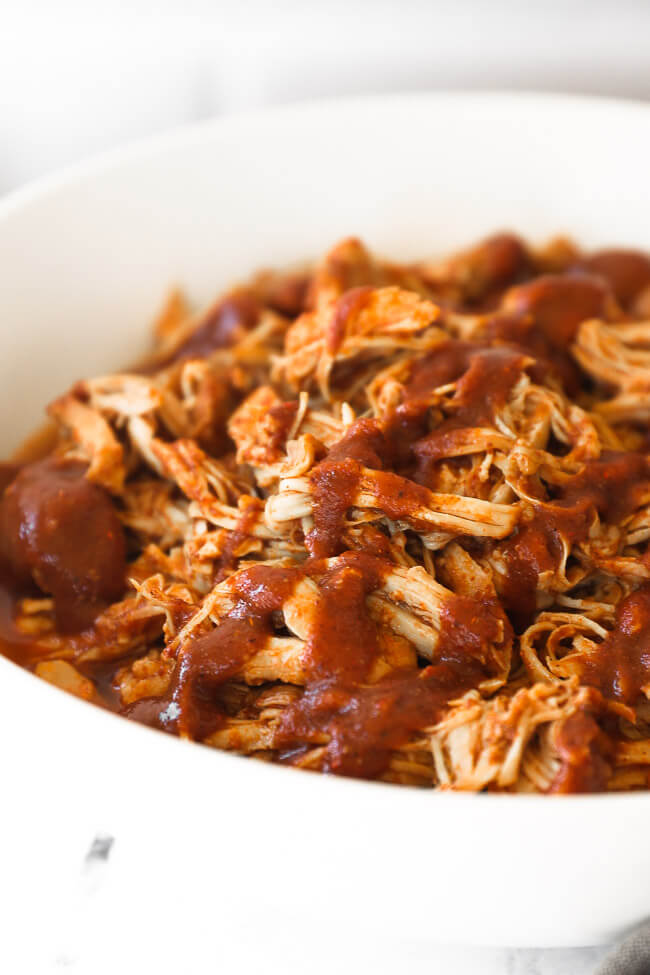 Close up angle of shredded chicken in a bowl topped with bbq sauce