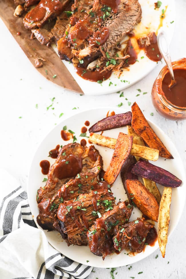 Sliced beef brisket on a plate with a side of sweet potato fries.