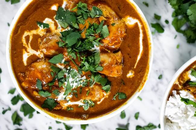 Instant pot butter chicken in a bowl with coconut milk drizzled on top and chopped fresh cilantro. 