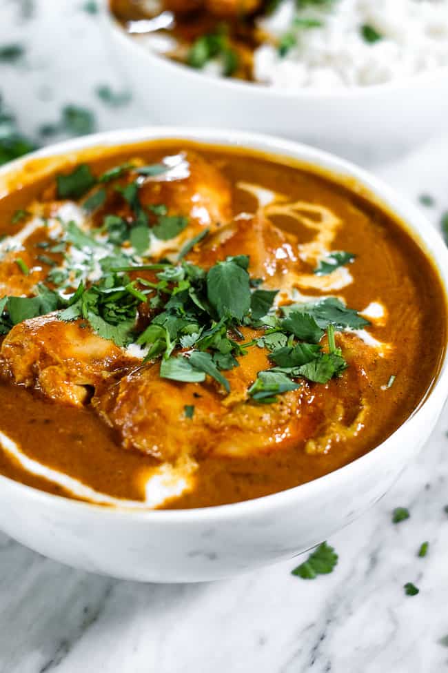 Angle shot of instant pot butter chicken in a bowl with coconut milk drizzled on top and fresh chopped cilantro. 