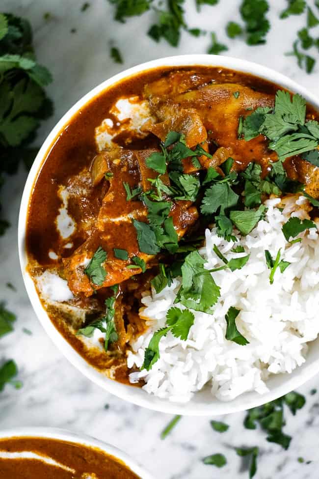 Instant pot butter chicken in a bowl served with white rice. Topped with a drizzle of coconut milk and fresh chopped cilantro. 