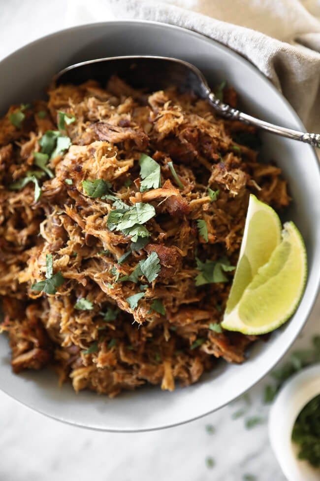 Instant pot carnitas in bowl with lime wedges and cilantro overhead vertical close up image