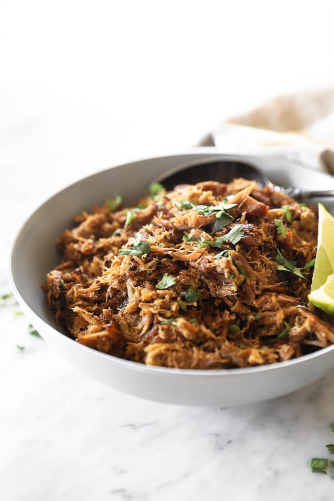 Instant pot carnitas in bowl with lime wedges and cilantro close up angle vertical image