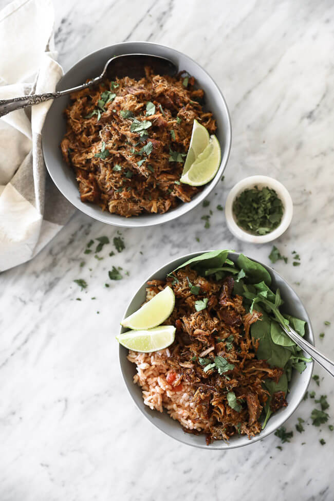 Instant pot carnitas in bowls with lime wedges, cilantro, rice and spinach overhead vertical image