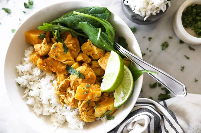 Instant pot chicken curry in bowl with rice, spinach and lime horizontal image