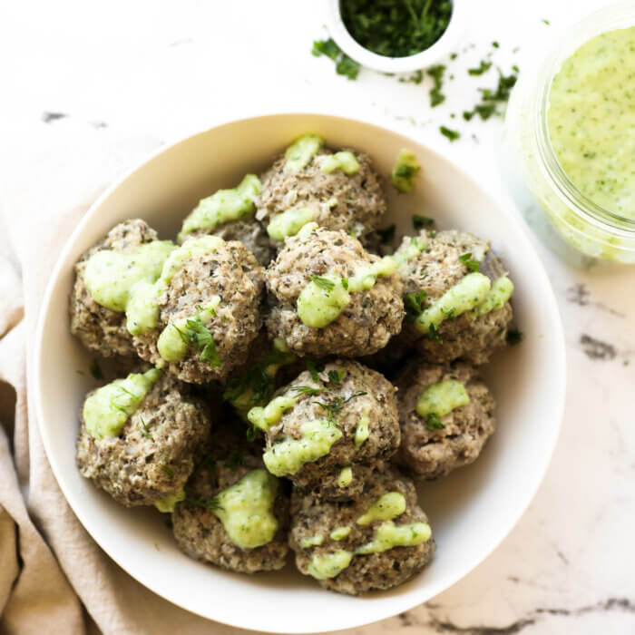 Overhead shot of instant pot greek meatballs in a bowl with green sauce drizzled on top