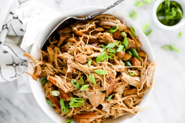 Horizontal image of instant pot honey garlic chicken in a bowl with a serving spoon, topped with chopped green onion. 