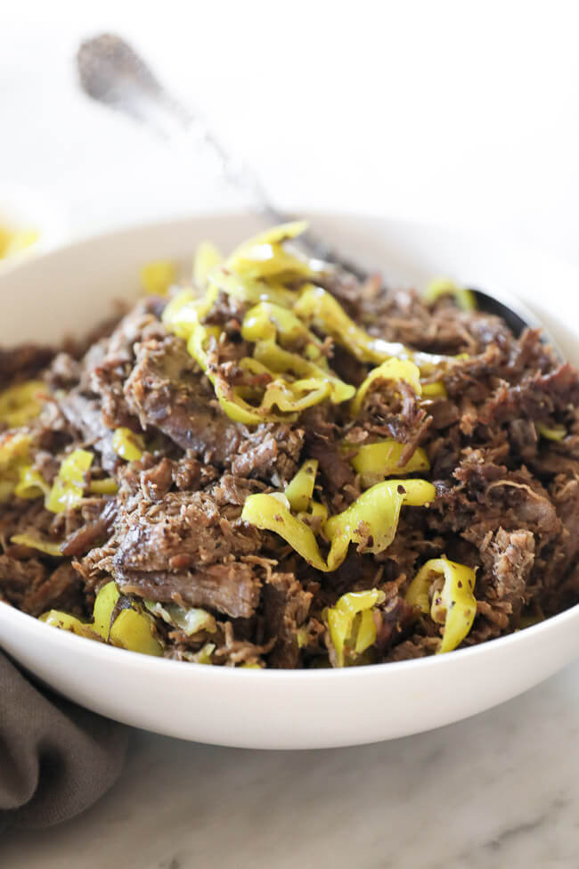Instant pot italian beef shredded in a bowl with peppers and spoon close up angle image