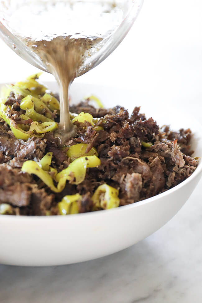Instant pot italian beef shredded in a bowl with peppers and dressing pouring in close up angle image