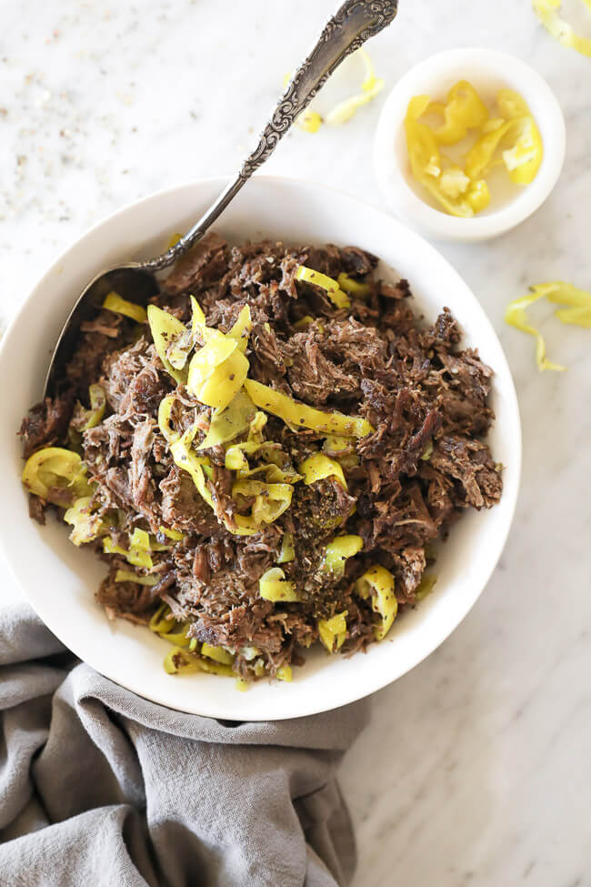 Instant pot italian beef shredded in a bowl with peppers and spoon vertical overhead image