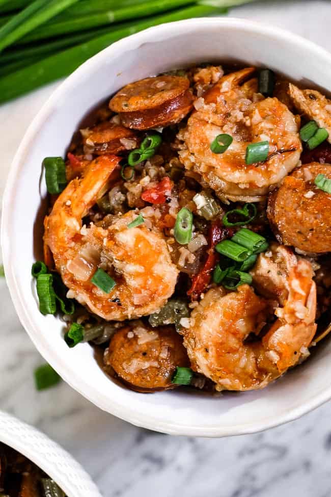 Close up of instant pot jambalaya served in a bowl with chopped green onion garnish and fork. 