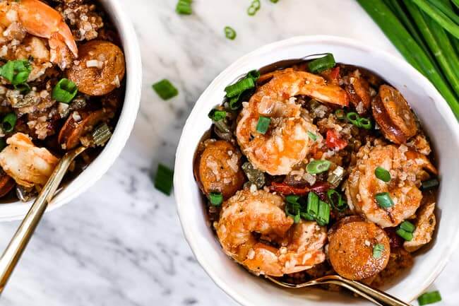 Instant pot jambalaya served in a couple bowls with chopped green onion garnish and forks. 