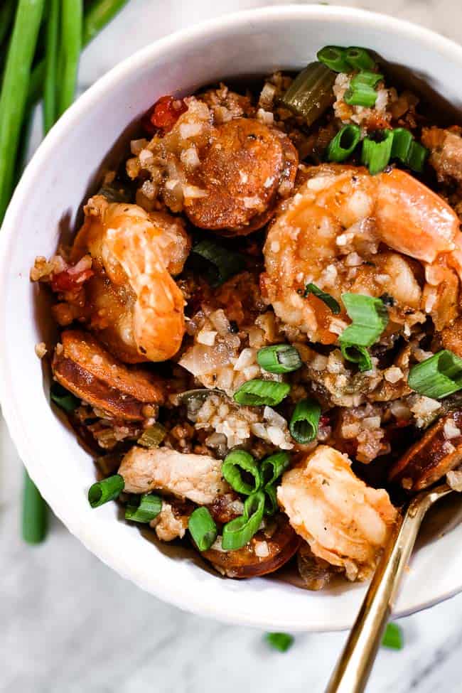 Close up of instant pot jambalaya served in a bowl with chopped green onion garnish and fork. 