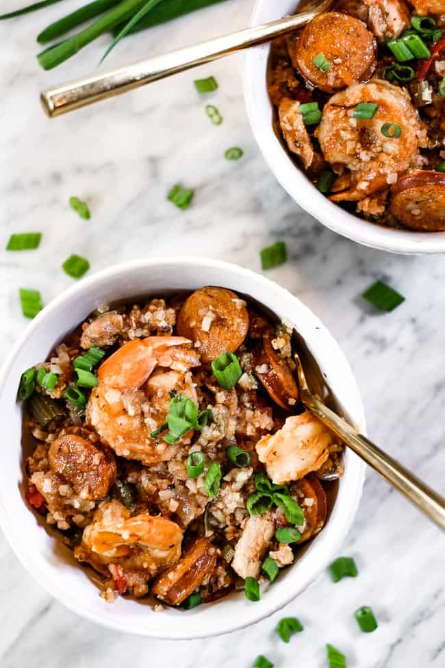 Instant pot jambalaya served in a couple bowls with chopped green onion garnish and forks. 