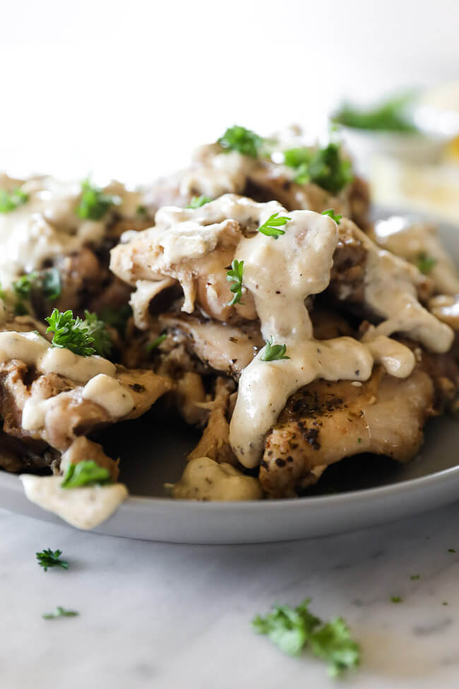 Chicken thighs stacked up on a plate and covered in creamy sauce topped with chopped parsley close up straight on vertical image 
