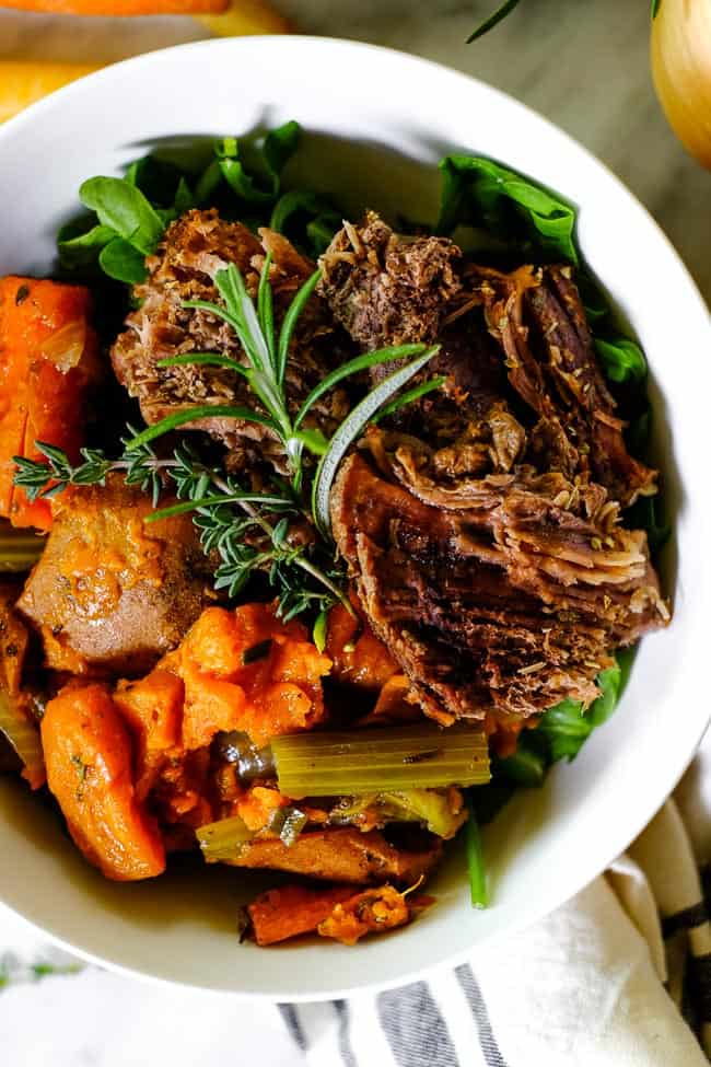 Instant Pot pot roast in a bowl with greens, sweet potato, onion, carrots, celery and fresh herbs. 