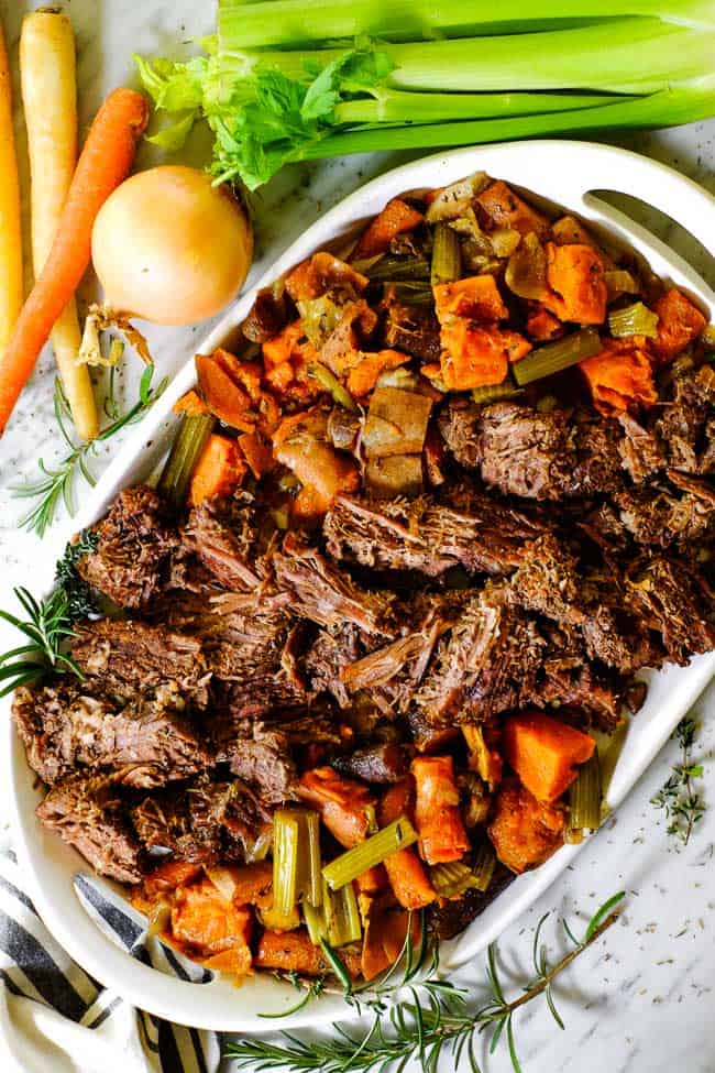 Instant Pot pot roast on a serving platter with sweet potato, carrots, onion, celery and fresh herbs. 