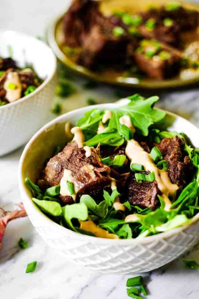 Instant pot short ribs served in a bowl with greens and topped with mayo sauce and chopped green onion.