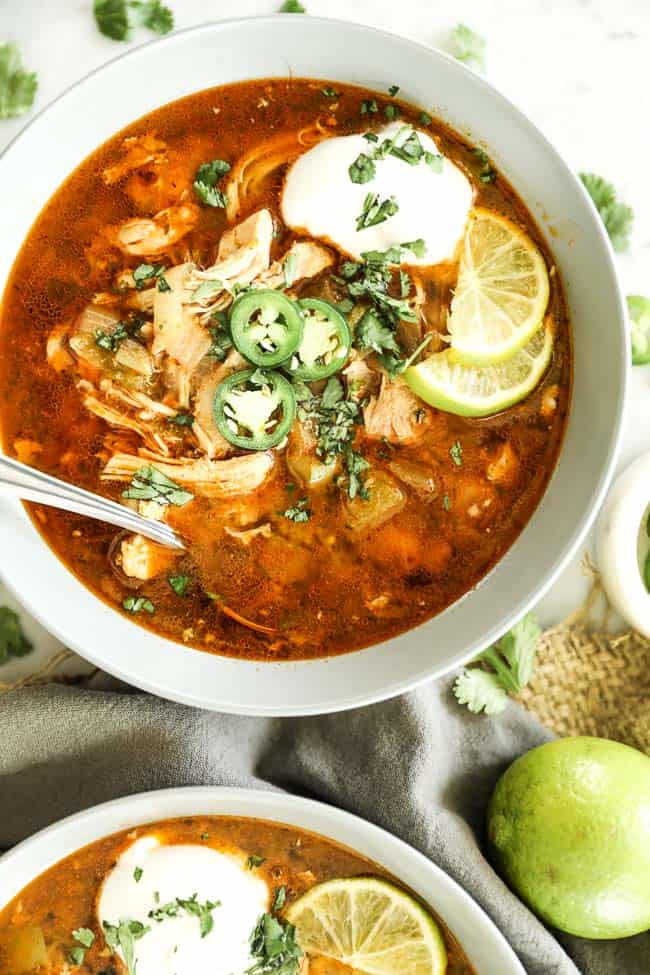 Instant pot white chicken chili vertical image with one bowl at top close up with toppings and spoon sticking out. 