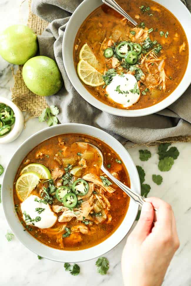 Instant pot white chicken chili vertical image with one bowl at bottom  with toppings and spoon sticking out. 