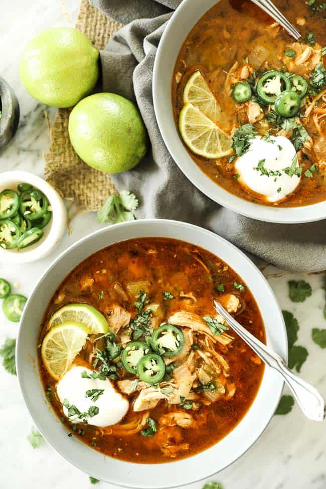 Instant pot white chicken chili vertical image with two bowls at bottom with toppings. Hand holding spoon at bottom. 