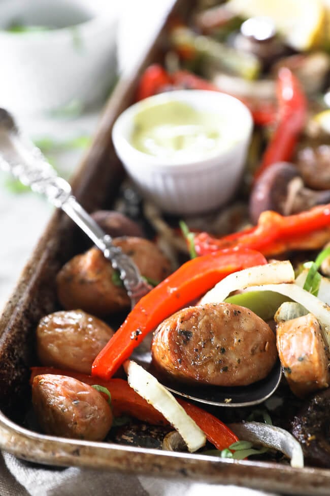 Vertical close up angled image of sheet pan filled with Italian sausage, bell peppers, onion and mushrooms. 