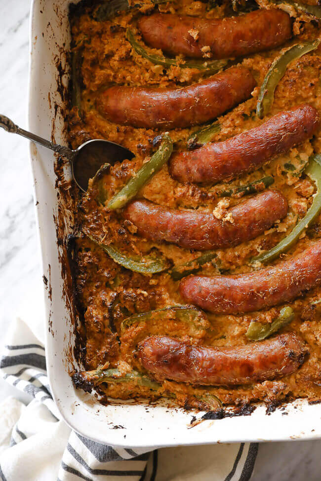 Sausages and bell peppers in a casserole dish over creamy cauliflower overhead vertical image close up