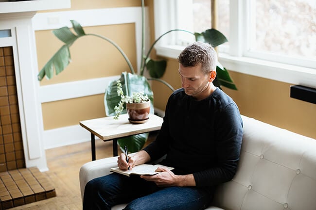 Justin Winn sitting on white couch journaling