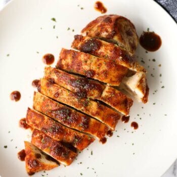 Sliced chicken breast on a plate with sauce drizzled on and around. Air fryer chicken breast cooked from frozen.