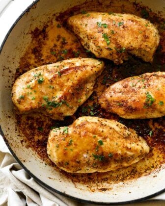 Image of a skillet with four chicken breasts cooked in a buttery sauce. Fresh parsley sprinkled on top.