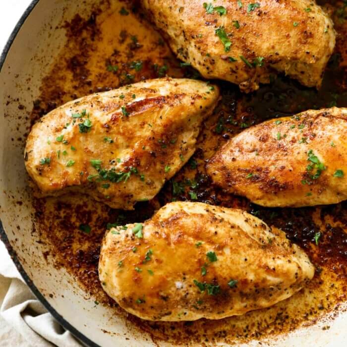Image of a skillet with four chicken breasts cooked in a buttery sauce. Fresh parsley sprinkled on top.