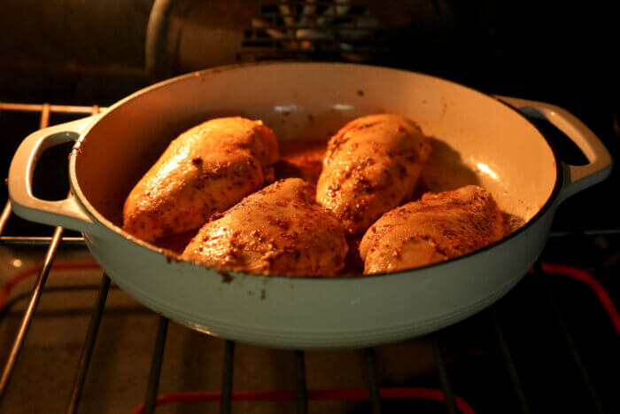 Four chicken breasts cooking in a skillet in the oven.