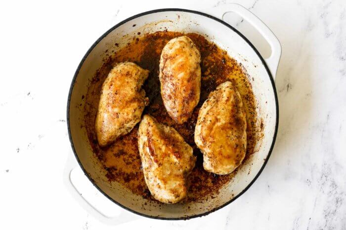 Horizontal image of four buttery chicken breasts cooked in a skillet.