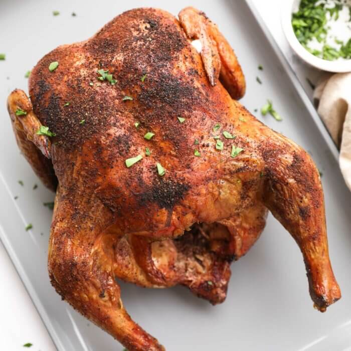cooked smoked whole chicken on a pan at an angle with chopped green garnish sprinkled on top