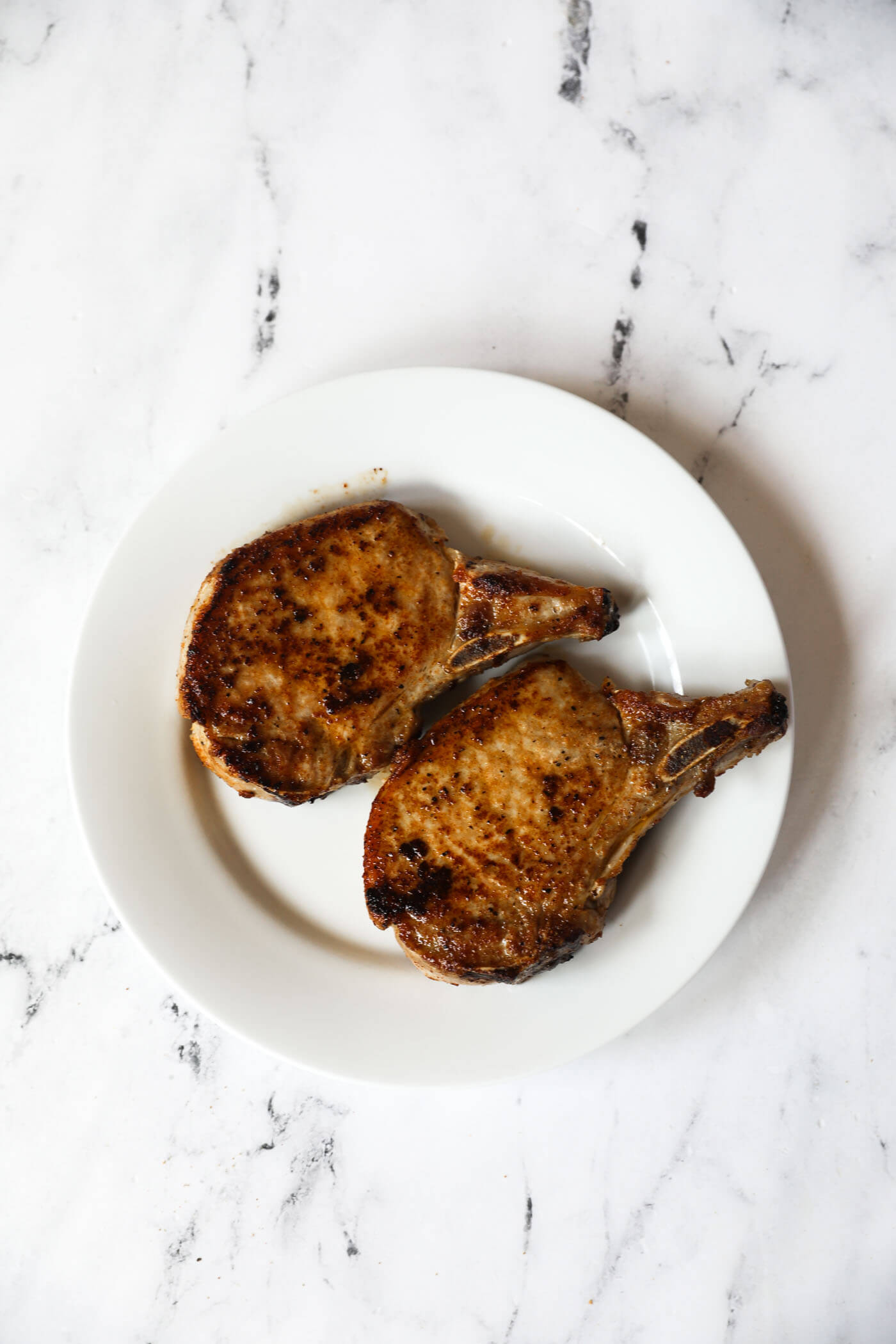 Two pork chops resting on a plate for five minutes after cooking.