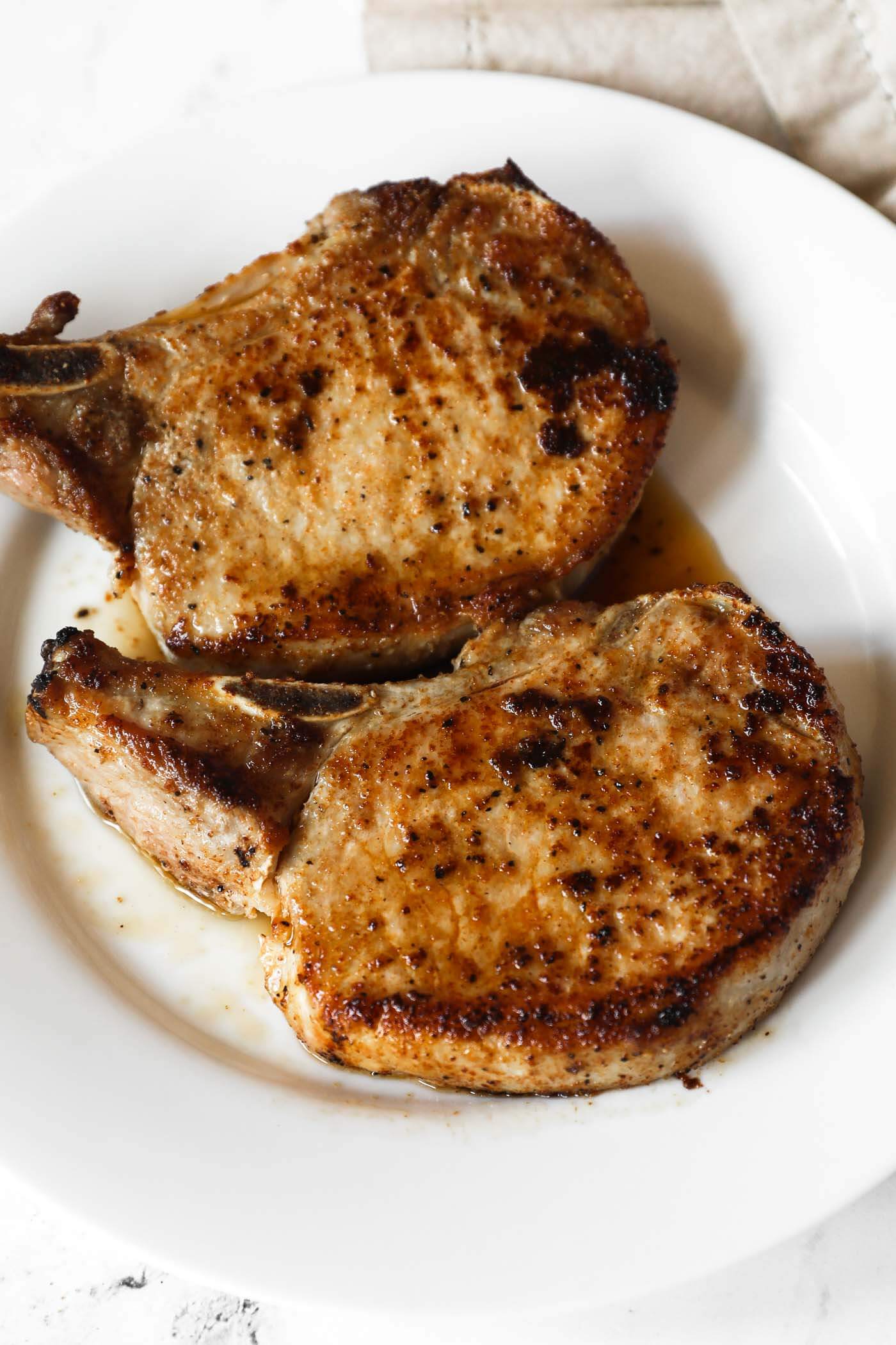 Close up angled shot of two pork chops on a plate after being cooked on a blacktop.