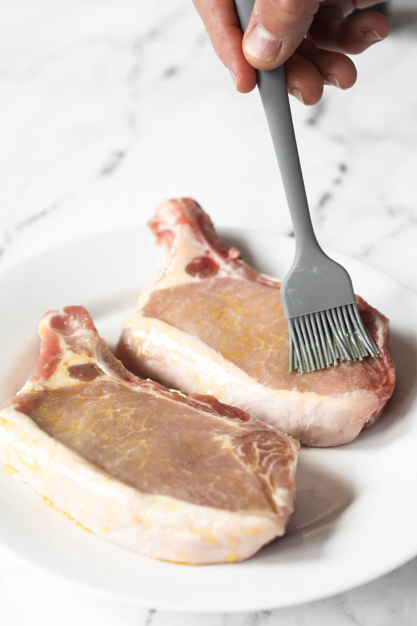 Using a brush to spread the oil all over two pork chops.